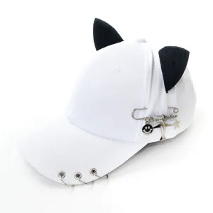 Detail shot of white baseball cap showing metal rings on brim and punk safety pin charms.