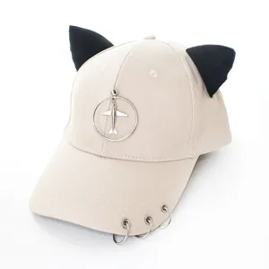 Détail de la casquette de baseball kaki avec oreilles de chat, pendentif avion et anneaux.