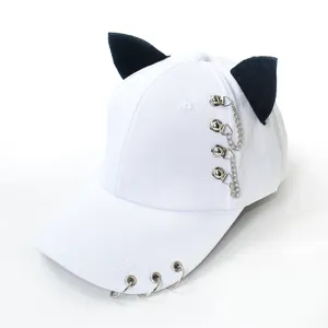 Détail de la casquette blanche avec oreilles de chat noires et anneaux métalliques.