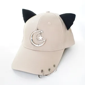 Détail d'une casquette beige avec oreilles de chat noires et breloque lune en métal