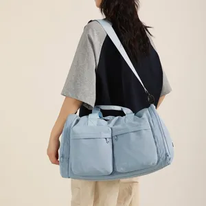 Grand sac de sport bleu clair porte sur l'epaule, montrant les details de voyage et de fitness.