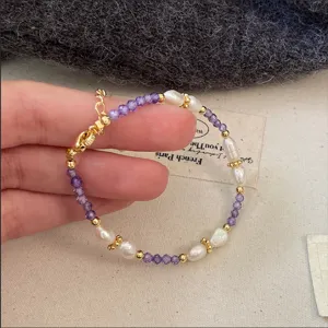 Vista macro detallada de una pulsera de piedras moradas y perlas barrocas sostenida a mano.