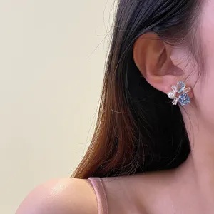 Dettaglio di orecchini a lobo in zircone colorato con pietre blu e perla su modella.