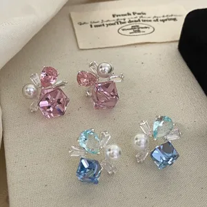 Primo piano di orecchini di zirconi rosa e blu con perle su sfondo di tessuto.
