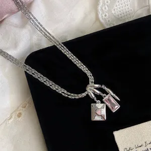 Makroansicht der silbernen dreilagigen Kette mit rosa Briefumschlag- und Zirkonia-Anhängern