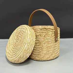 Vista detallada de una cesta de regalo cilíndrica de paja tejida con asa de cuero marrón