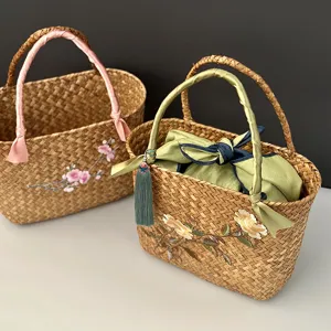 Détail d'un panier en paille tressée main avec broderie florale et anses en ruban de soie.