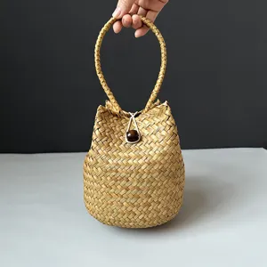 Hand holding a natural handmade seagrass woven bucket bag with wooden bead closure.
