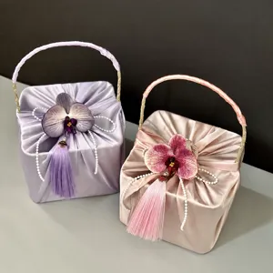 Satin gift box with orchid and tassel handle, elegant packaging basket for wedding party.