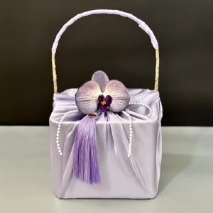 Purple satin gift box with elegant orchid, tassel, and pearl chain handle for weddings.