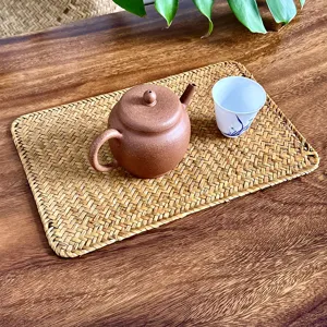 Detailed shot of handmade woven straw placemat on wooden table with teacup and teapot prop.