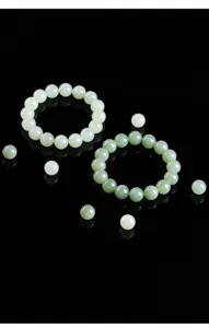 Close-up of polished natural green Hetian jade beads and bracelets on a black reflective surface.