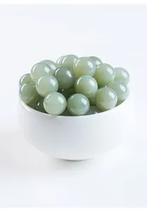 Macro view of polished light green round Hetian jade beads in a white ceramic bowl