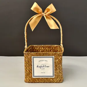 Handwoven square straw gift basket featuring a large golden satin bow and a gift card