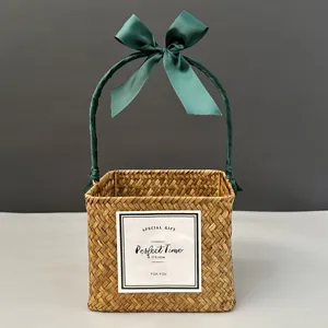 Detail of square hand-woven straw gift basket featuring an elegant green satin ribbon bow