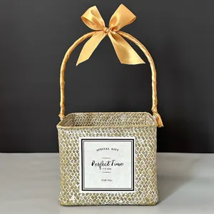 Detail view of a square hand-woven straw gift basket with an elegant golden bow handle.