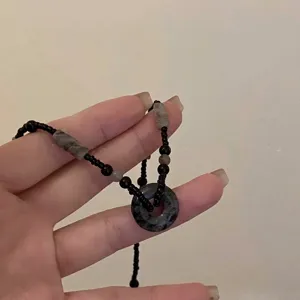 Detailopname van een hand die een kralenketting in inktstijl met marmeren hanger vasthoudt.