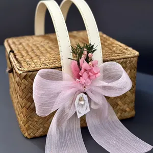 Détail du panier cadeau en paille tissée, nœud rose et fleurs séchées, poignée cuir.