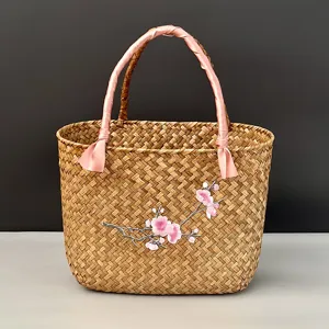 Détail de panier en paille tissée, poignée ruban rose et broderie de fleurs de prunier.