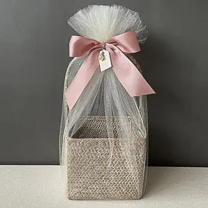 Detalle de cesta de regalo de bambú trenzado con tul blanco y lazo rosa suave