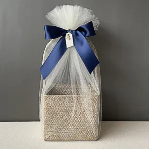 Primer plano de cesta de regalo tejida cuadrada con tul blanco y lazo azul marino elegante
