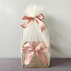 Detail shot of gold wire gift basket decorated with white tulle mesh and pink satin bows.