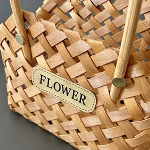 Detailaufnahme eines handgewebten Blumenkorbs im Waldstil mit dekorativem Lederetikett.
