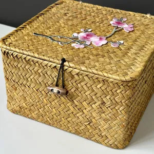 Detailansicht einer handgeflochtenen Strohbox mit pinker Blumenstickerei und Holzknopfverschluss