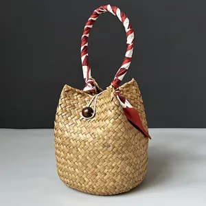 Handmade natural seagrass straw bucket bag featuring a decorative red and white scarf handle