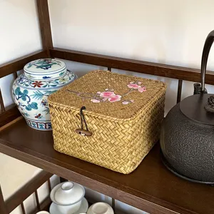 Handgeflochtene Aufbewahrungsbox aus Stroh mit floraler Stickerei auf Holzregal