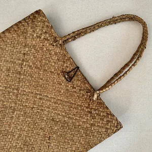 Close-up detail of natural woven straw handbag texture, featuring braided handles and wooden toggle.