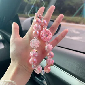 Dettaglio della catena per cellulare rosa con donut, perle iridescenti dipinte a mano.