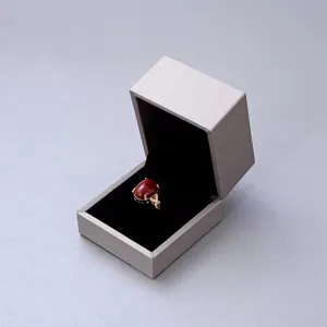 Elegante gouden ring met ovale rode edelsteen in een minimalistische grijze geschenkdoos