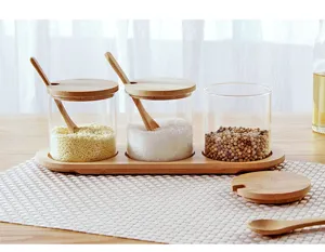 Conjunto de tarros de especias de vidrio transparente con tapa, cuchara y bandeja de madera.
