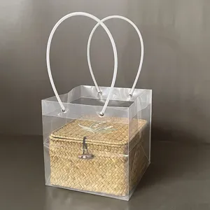 Detailed view of hand-woven straw gift box with floral embroidery inside clear PVC tote bag