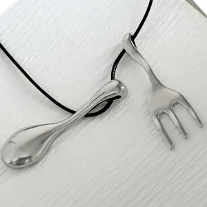 Close-up of unique silver fork and spoon pendants on a minimalist black necklace cord