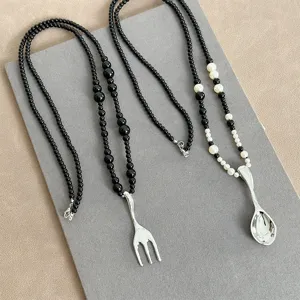 Close-up view of creative silver fork and spoon pendants with black and white pearl beads