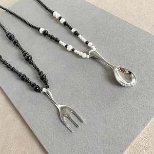 Close-up of creative spoon and fork pendants on black and white beaded necklaces.