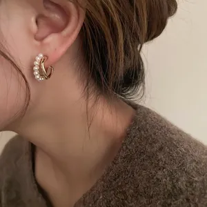 Elegante C-vormige dubbellaagse gedraaide gouden oorbellen met parels op het model.
