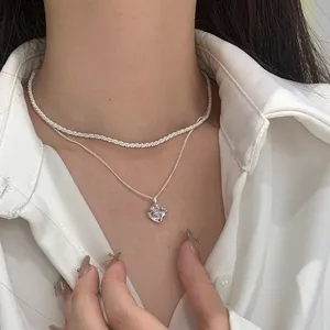 Detail view of a sparkling layered silver necklace with a clear geometric pendant.
