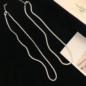 Close-up detail of two sparkling textured silver chain necklaces on black background