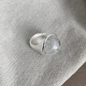 Dettaglio di un anello in argento con una grande pietra di cristallo a cupola trasparente.