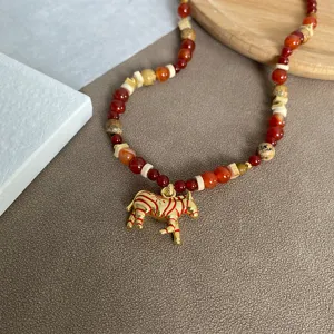 Detail van een gouden zebra hanger met rode strepen aan een boho kralen halsketting.