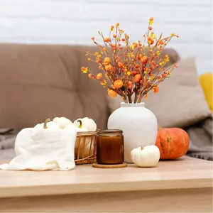 Detailed view of autumn artificial pumpkin berry branches in a stylish white ceramic vase.