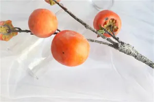 Close-up detail of a realistic artificial persimmon branch with frosted orange fruits
