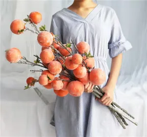 Artificial frosted persimmon fruit branches held by a model for indoor home decor