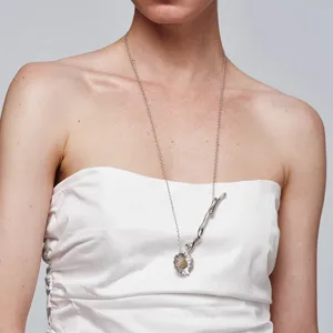 Close-up van een elegante madeliefjesketting met een zilveren takdetail gedragen door een model