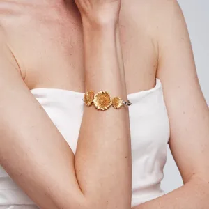 Prachtige gouden madeliefjes armband getoond op de pols van een elegant vrouwelijk model.