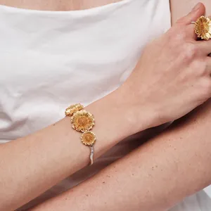 Gedetailleerde close-up van een gouden zonnebloem armband en ring op de arm van een model