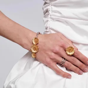 Detailopname van een gouden zonnebloem sieradenset met armband en ring op witte jurk